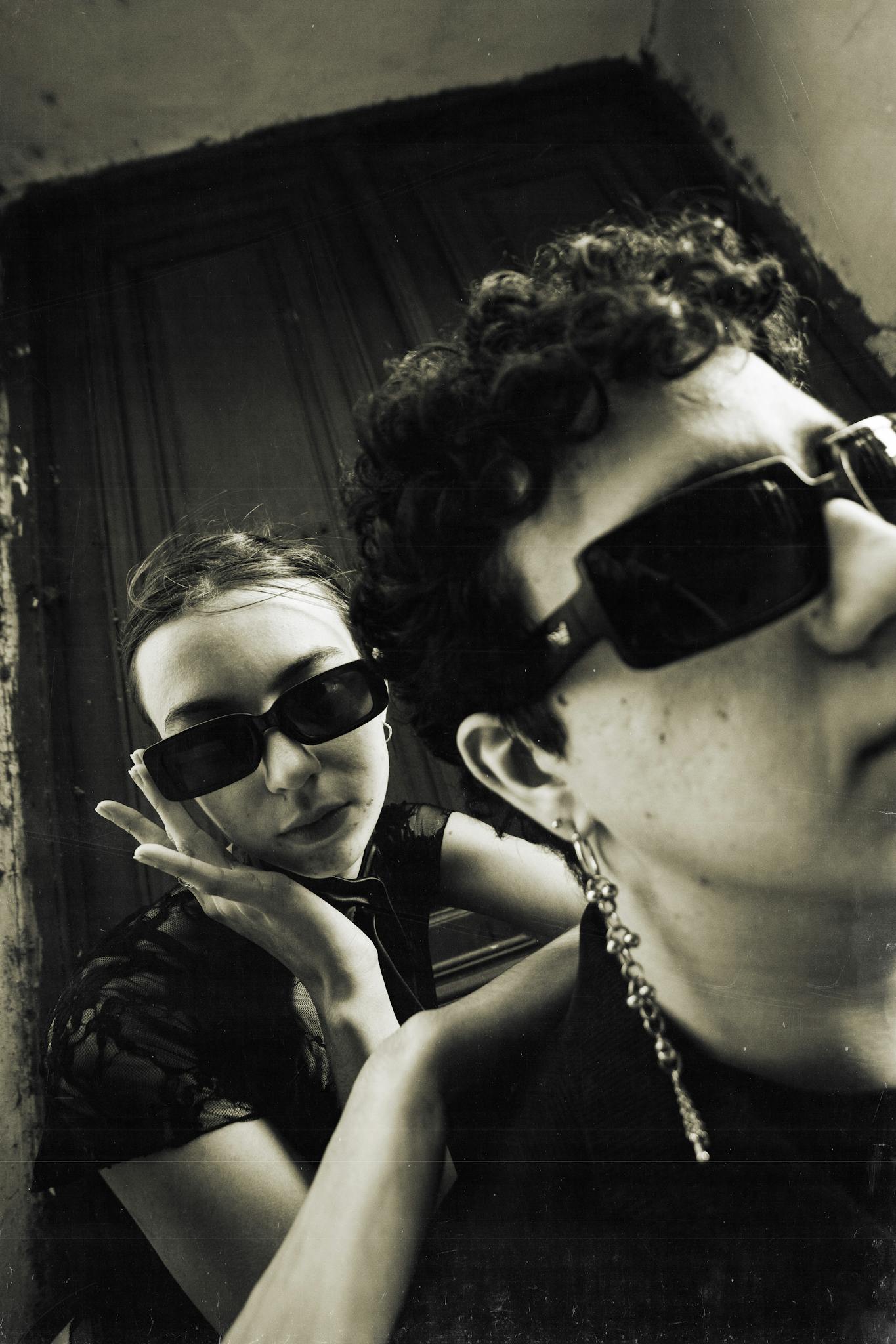 Two stylish adults in sunglasses posing in an artistic black and white photograph.